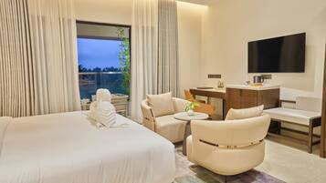 A hotel room with a large bed, a desk, a chair, a television, and a view of the outdoors.