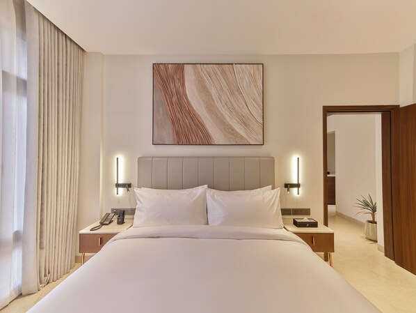Quarto de hotel com cama grande, mesas de cabeceira, telefone, obra de arte na parede e planta em vaso.