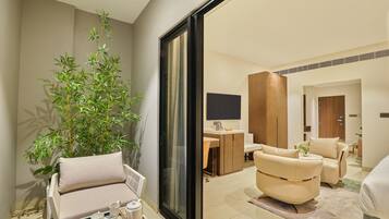Una habitación de hotel moderna con sofá, sillón y zona de comedor con una bandeja de desayuno.