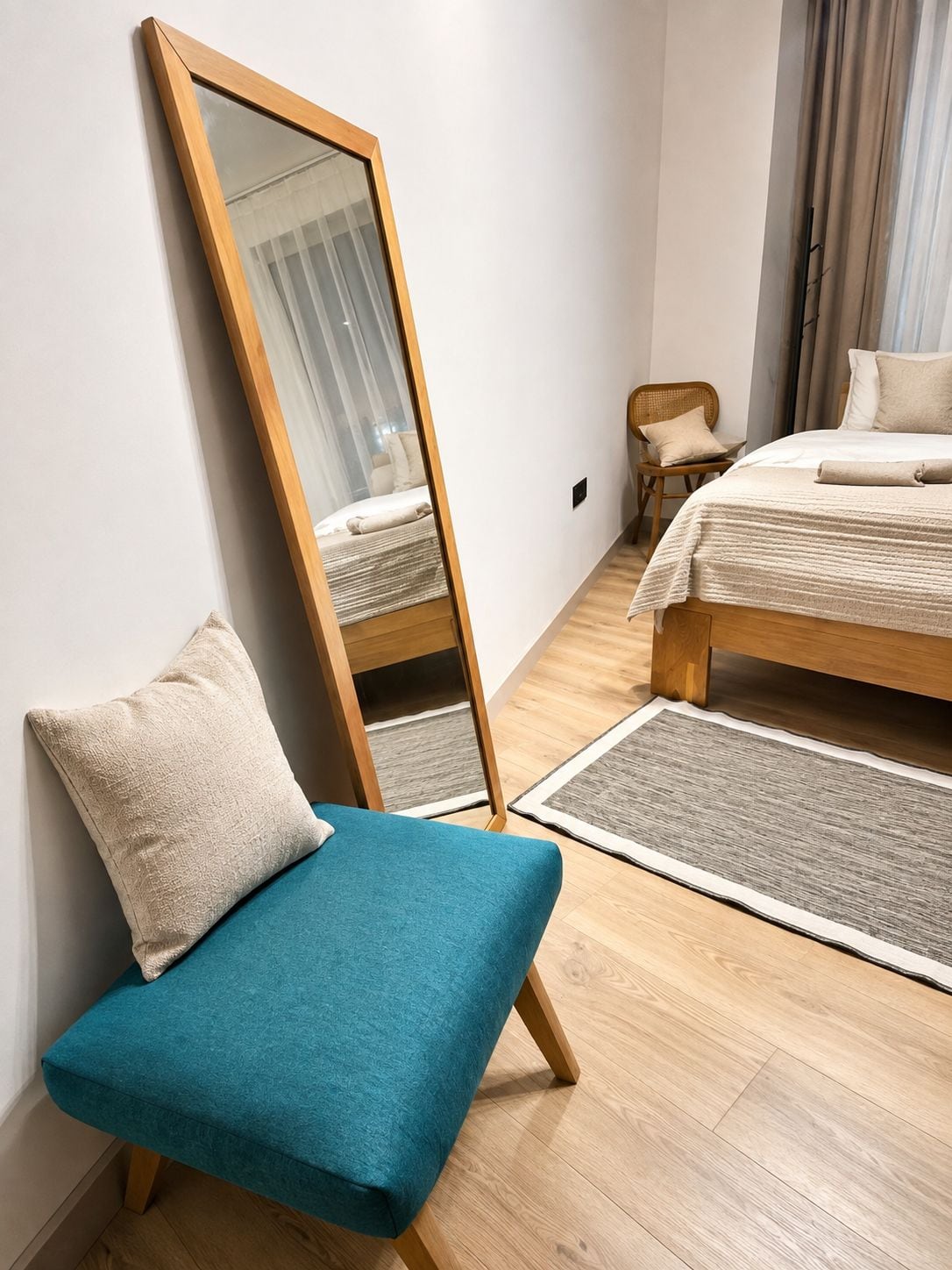 A bedroom with a bed, a chair, a large mirror, and a rug.