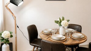 Uma sala de jantar com mesa redonda posta para quatro pessoas, rodeada por cadeiras de couro, um abajur e uma placa emoldurada acima.