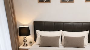 Cama bem arrumada com colcha branca, cabeceira escura e abajur.