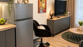 Una cocina moderna con refrigerador incorporado, un comedor con mesa redonda y sillas, una silla negra y un televisor de pantalla plana sobre un pedestal de madera.