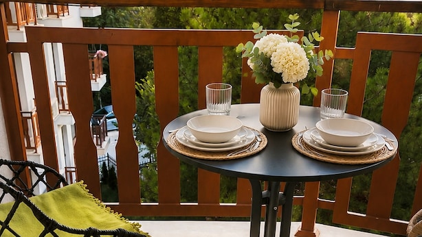 Varanda com mesa redonda posta para refeições, uma cadeira com almofada verde e planta em vaso.