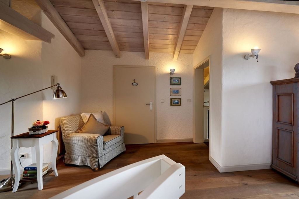 A cozy room with a checkered sofa, a white bedside table with books, a lamp, and a wooden cabinet.