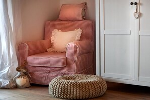 Ein gemusterter Sessel mit Kissen, ein kleiner Hocker und eine weiße Kommode mit herzförmiger Dekoration.