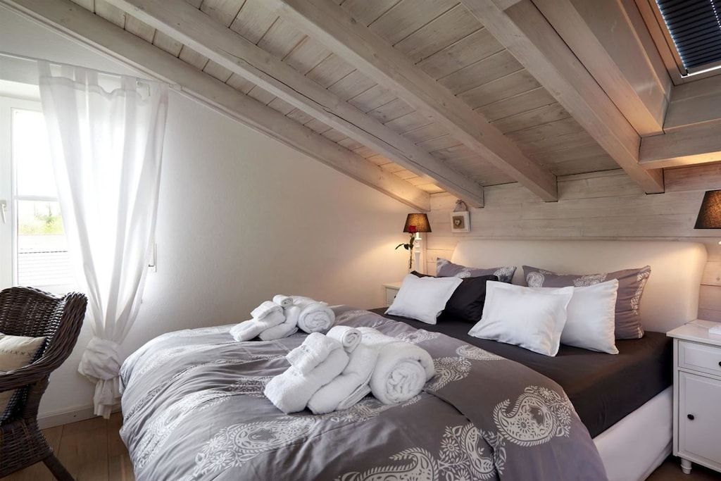 A bedroom with a bed, pillows, a nightstand, a lamp, and a chair.
