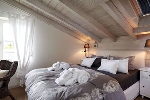 Ein Schlafzimmer mit einem Bett, Kissen, einem Nachttisch, einer Lampe und einem Sessel.