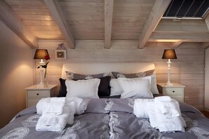 Ein Schlafzimmer mit Holzboden, einem Bett mit grauer Bettwäsche, zwei Nachttischen mit Lampen und einem Beistelltisch mit Blumen.