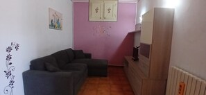 Una sala de estar con un sofá gris, una pared rosa y un mueble de madera con un televisor.