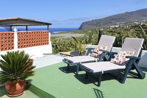 Een terras met twee loungestoelen, een plant in pot en uitzicht op zee en heuvels.