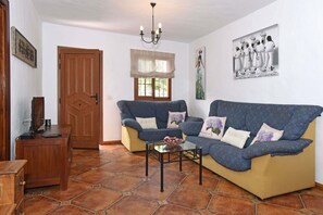 A living room with two sofas, a coffee table, a wooden cabinet, a door, and a window with a valance. - Cozy house with garden and sea views (Tazacorte)