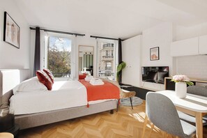 Quarto de hotel moderno com uma cama grande, uma escrivaninha, uma televisão e vista para a cidade.