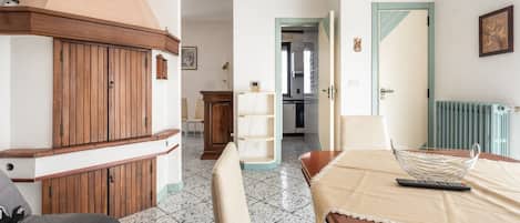 Habitación de hotel con una cama, un armario de madera, una mesa de comedor y una cocina visible a través de un umbral abierto.