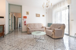 A room with a beige sofa, a round table, and a chandelier. There is a fire extinguisher on the wall. - Holiday Home - Matino (Matino)