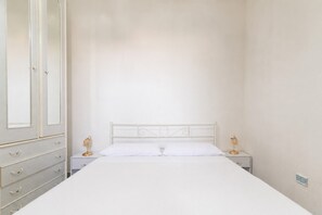 A bedroom with a white bed, a nightstand with a lamp, and a wardrobe. - Holiday Home - Matino (Matino)