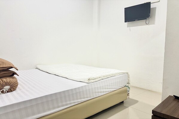 A single bed with a white mattress and a beige headboard, a small bedside table, and a wall-mounted TV. - Cozy Solo Room at Medina House (Banda Aceh)
