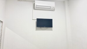 A white wall with a white air conditioning unit and a dark-colored object, possibly a television or monitor, mounted below it. - Cozy Solo Room at Medina House (Banda Aceh)
