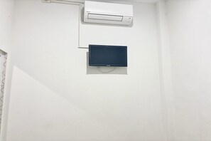 Una parete bianca con un condizionatore bianco e un oggetto scuro, probabilmente un televisore o un monitor, montato sotto.