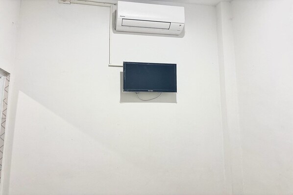 Eine weiße Wand mit einer weißen Klimaanlage und einem dunklen Gegenstand, vermutlich ein Fernseher oder Monitor, der darunter angebracht ist.