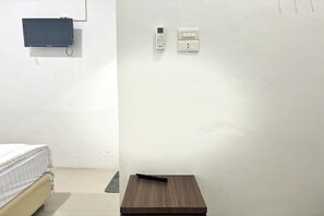 Una stanza con un letto, un tavolino, una TV a parete e un termostato.