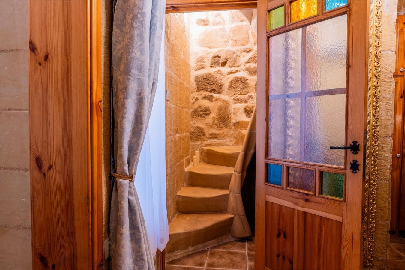 Una porta in legno con un vetro, un muro in pietra e una scala che conduce a un piano superiore.