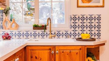Una cucina con un piano di lavoro bianco, un armadietto in legno, un lavello con un rubinetto dorato e uno schienale decorato.