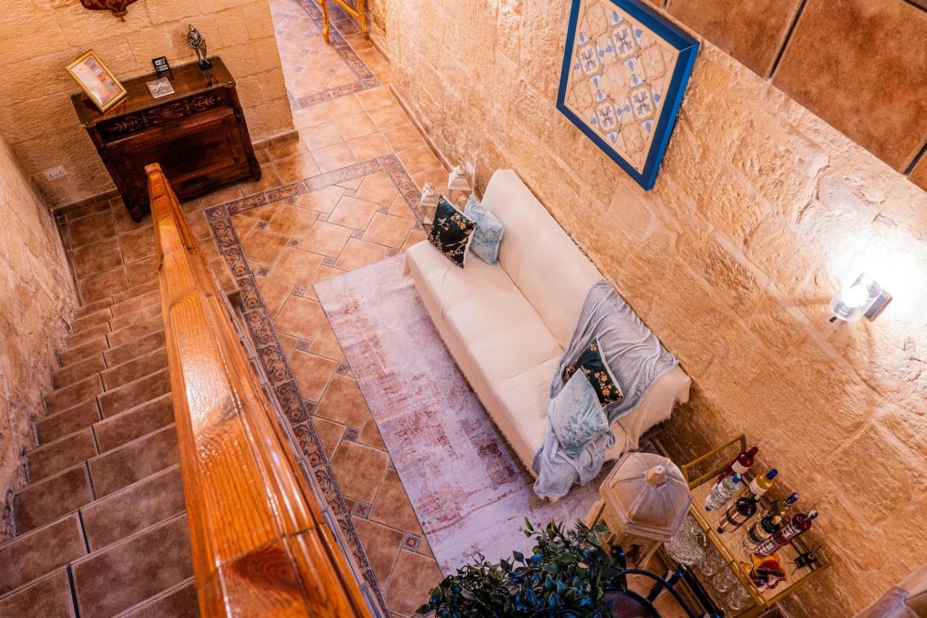 Un hall d’hôtel avec un escalier, un canapé avec des coussins, une petite table avec des bouteilles et un élément décoratif mural.