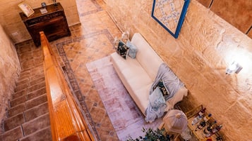 Un hall d’hôtel avec un escalier, un canapé avec des coussins, une petite table avec des bouteilles et un élément décoratif mural.