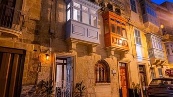 Un edificio storico con facciata in pietra, una porta in legno e un balcone con ringhiera in ferro battuto.