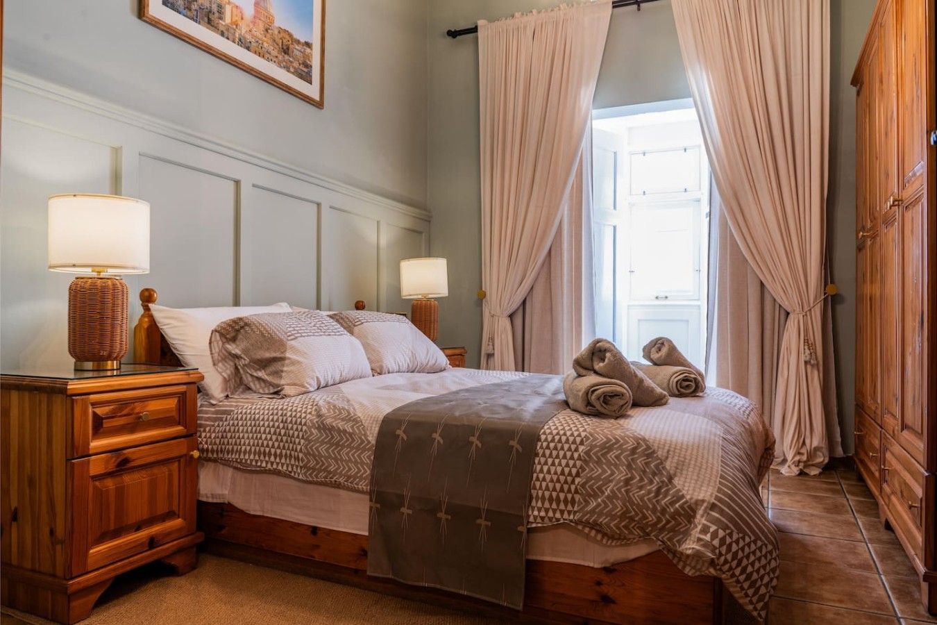 Un letto rifatto con cura, con una coperta a motivi decorativi, due abat-jour e una coppia di asciugamani sul letto.