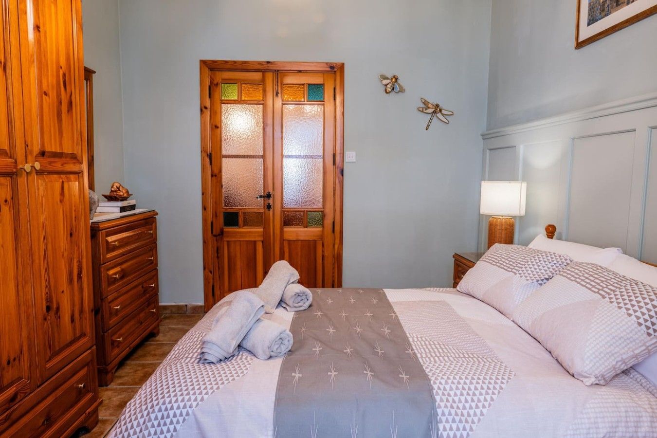 Una camera da letto con un armadio in legno, un letto con biancheria a motivi, un comodino con una lampada e una porta con pannelli trasparenti.