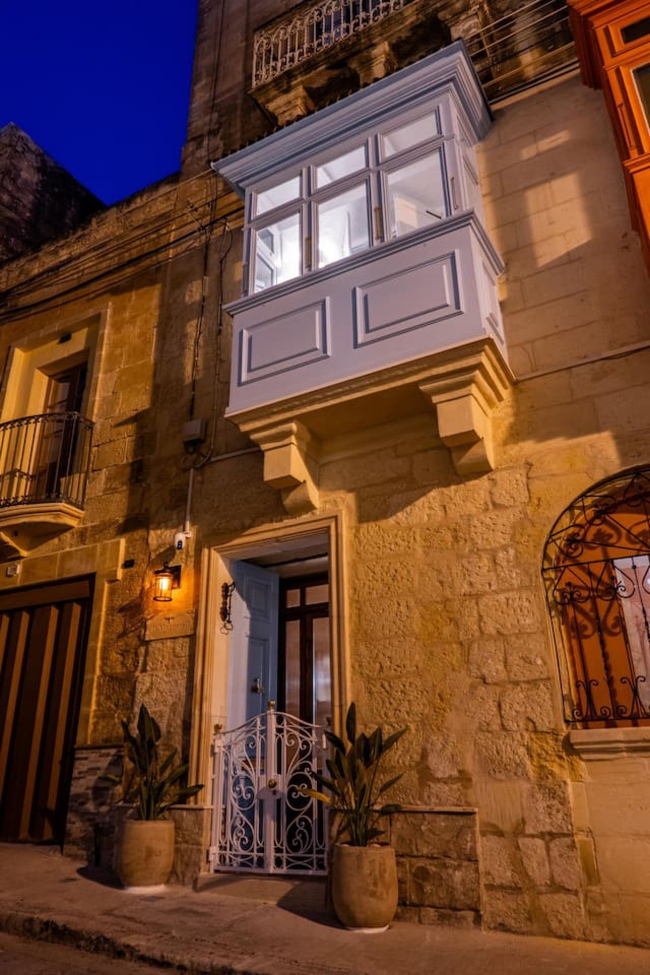 Un edificio in pietra con un balcone, un cancello e piante in vaso.