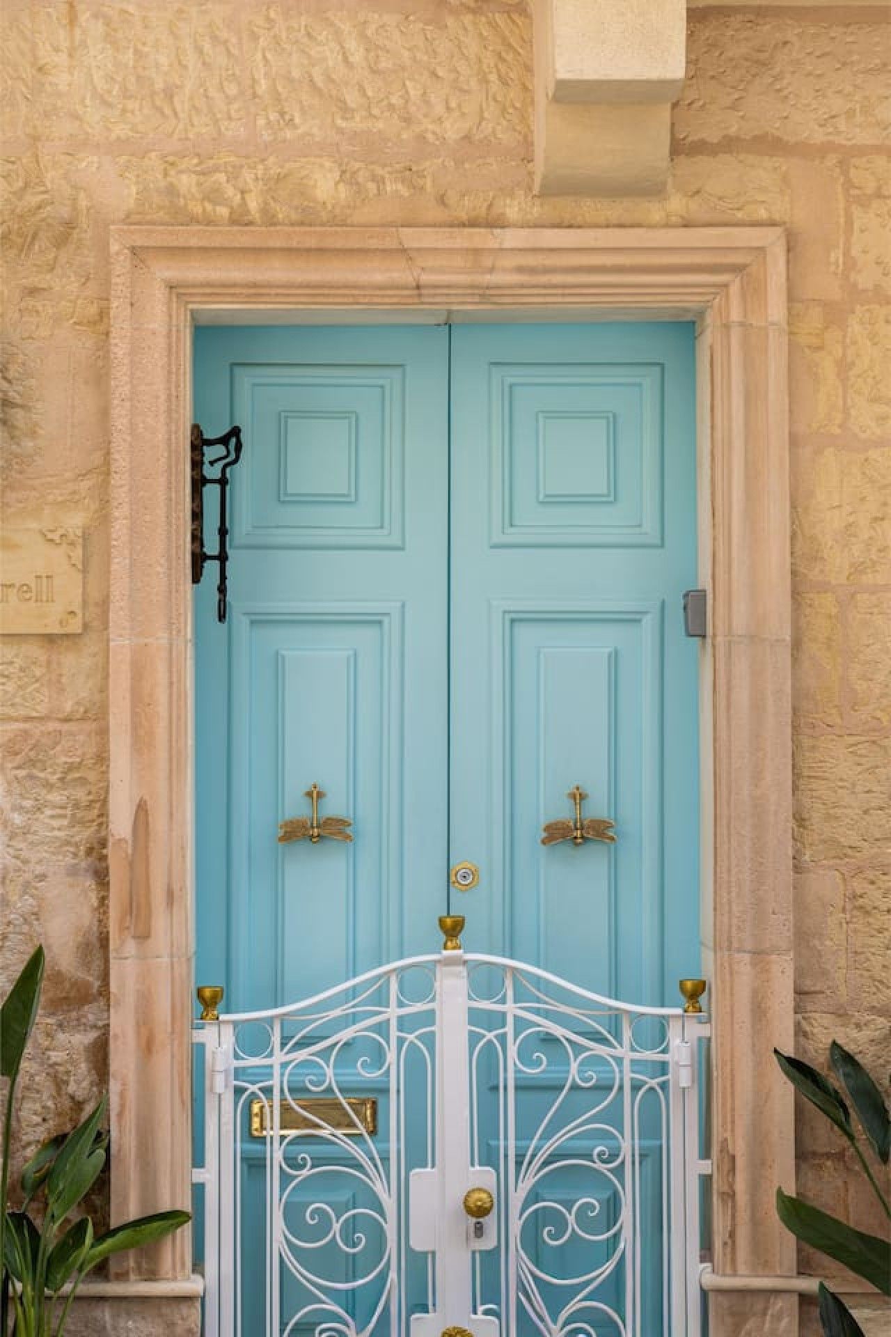 Una porta azzurra con un cancello in metallo bianco, incastonata in un muro di pietra.
