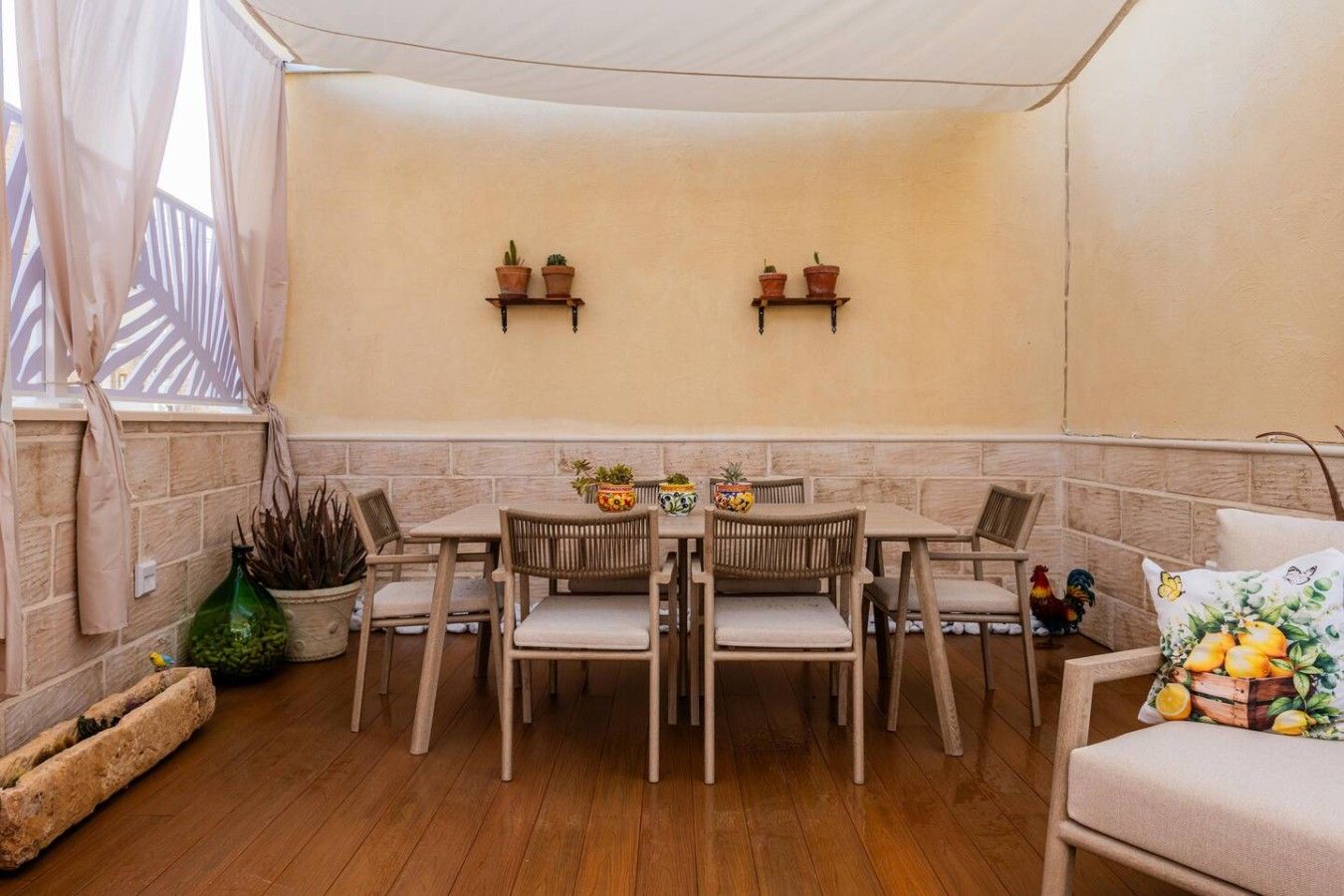 Una zona patio accogliente con tavolo e sedie, piante in vaso e luci a parete.