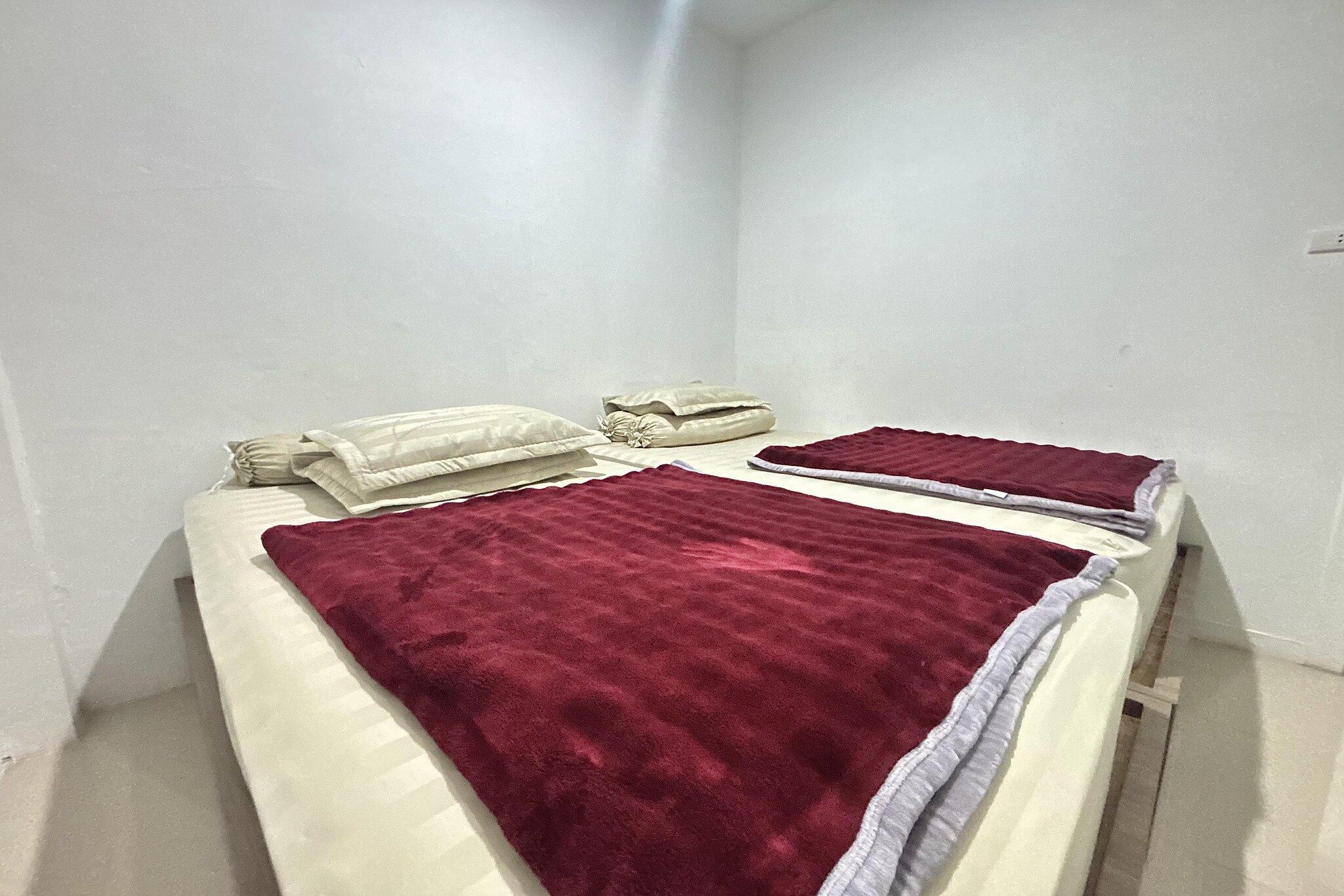 Un lit simple avec une couverture rouge et des oreillers, dans une pièce aux murs blancs.