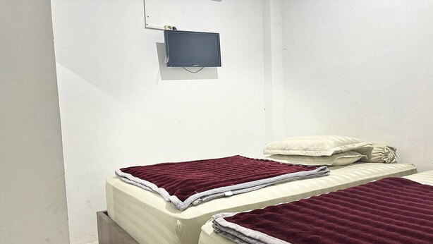 Un alojamiento pequeño de una sola habitación con dos camas, cada una con una manta y almohadas rojas.