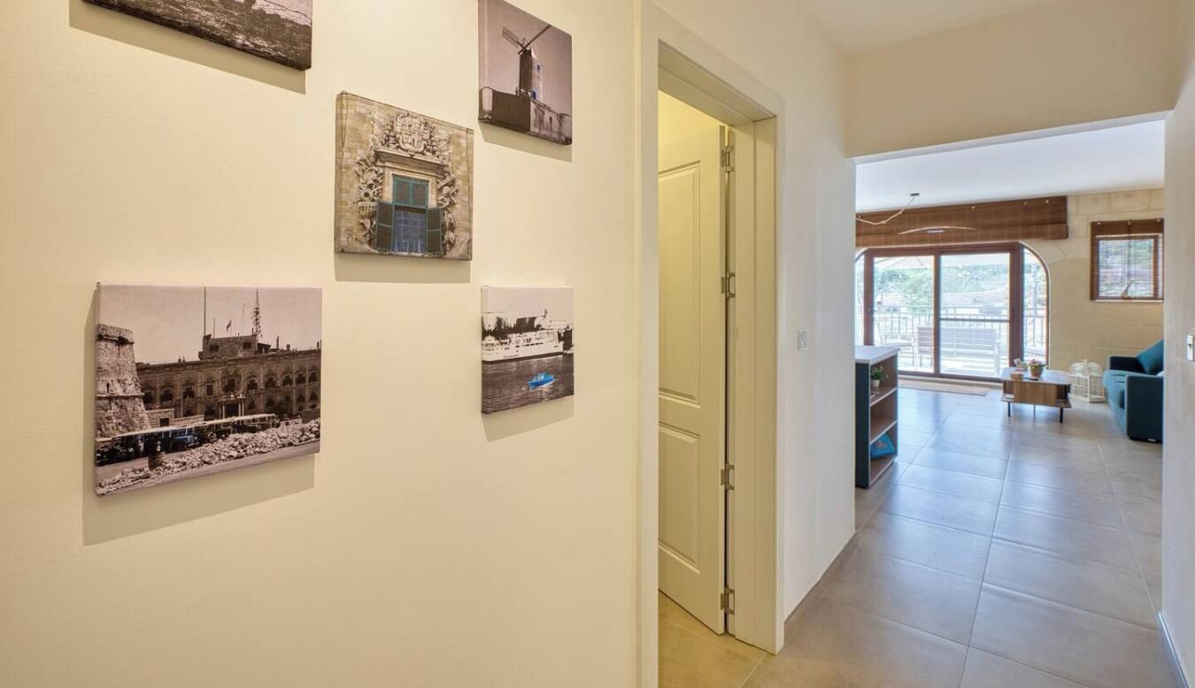 Un couloir orné d’une série de photographies encadrées, une porte donnant sur une pièce et une vue sur un salon avec un canapé et une fenêtre.