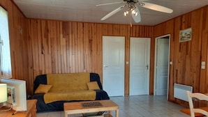 Una habitación con pared de paneles de madera, un sofá, una mesa de centro, un ventilador de techo y una puerta.