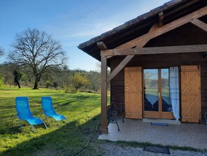 A wooden building with a covered porch, two blue chairs, and a bench.