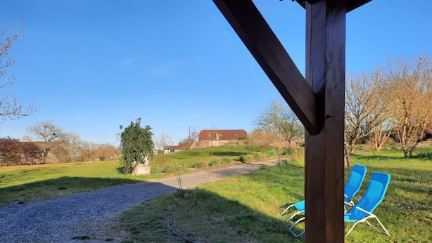 Un espacio al aire libre cubierto con un sendero de grava que conduce a un campo de césped, un banco y dos sillas azules.