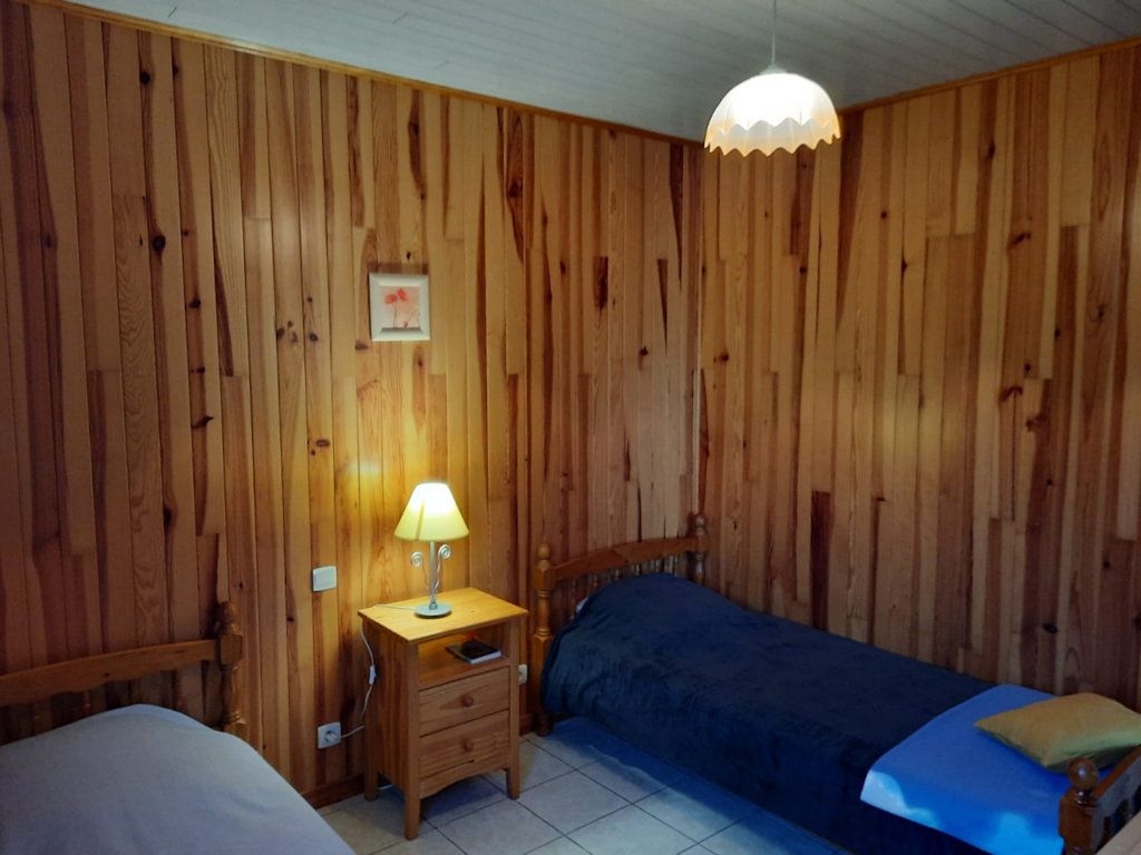 A room with wooden panel walls, a single bed with a blue blanket, a nightstand with a lamp, and a hanging light fixture.