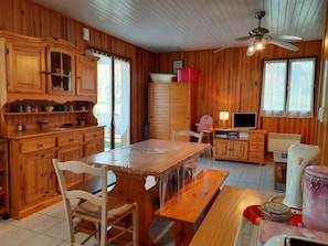 A wooden interior with a dining table, chairs, cabinets, a television, and a ceiling fan.