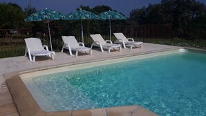 Una piscina con agua cristalina, rodeada de sillas de descanso blancas y dos sombrillas.