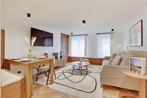 Ein modernes Wohnzimmer mit einem Holzesstisch, einer Couch und einem an der Wand befestigten Fernseher.