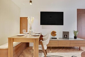 Ein moderner Essbereich mit Holztisch, weißen Stühlen, einem flachbildfernseher an der Wand und einer kleinen Vitrine mit Dekoration.