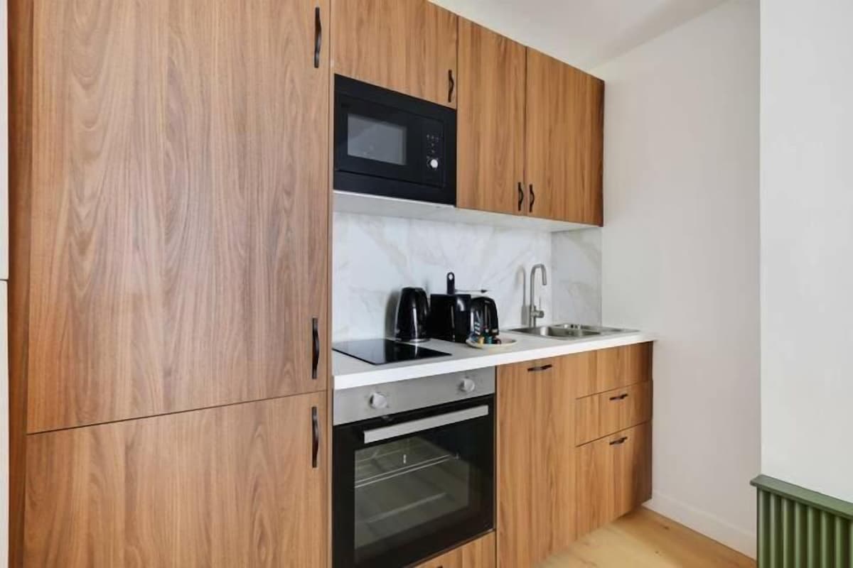 Cocina compacta con armarios de madera, microondas, cafetera y horno integrado.