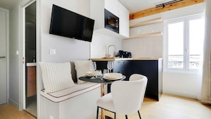 Un espace de vie compact comprenant un coin cuisine, un espace repas avec une table et des chaises, et un téléviseur fixé au mur.