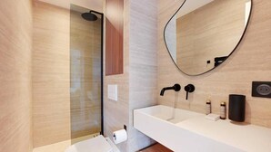 Une salle de bain moderne avec une douche à parois de verre, un lavabo blanc doté d’un robinet noir et un miroir rond accroché au mur.
