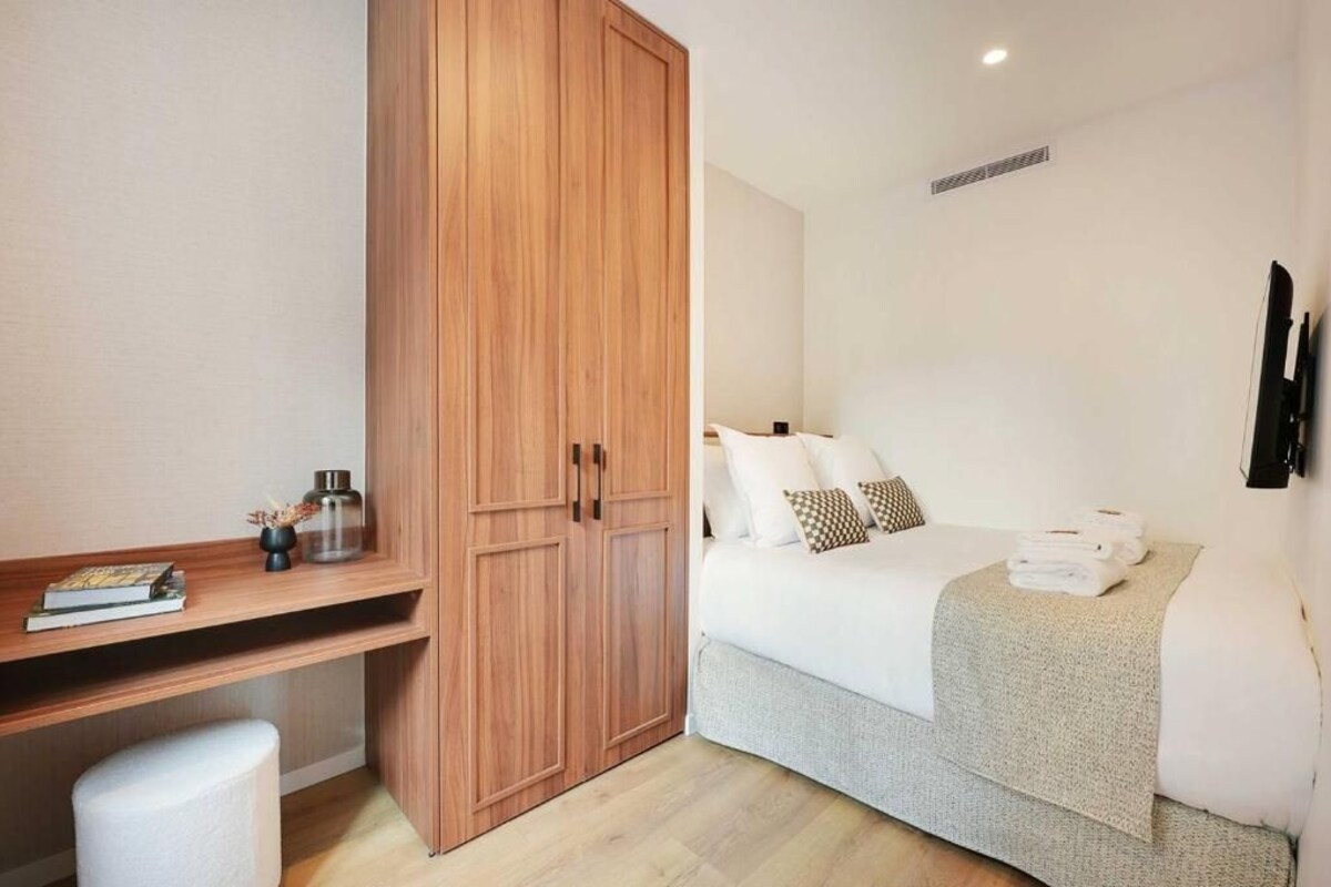 Habitación de hotel con cama, armario, escritorio con lámpara y televisor de pantalla plana.